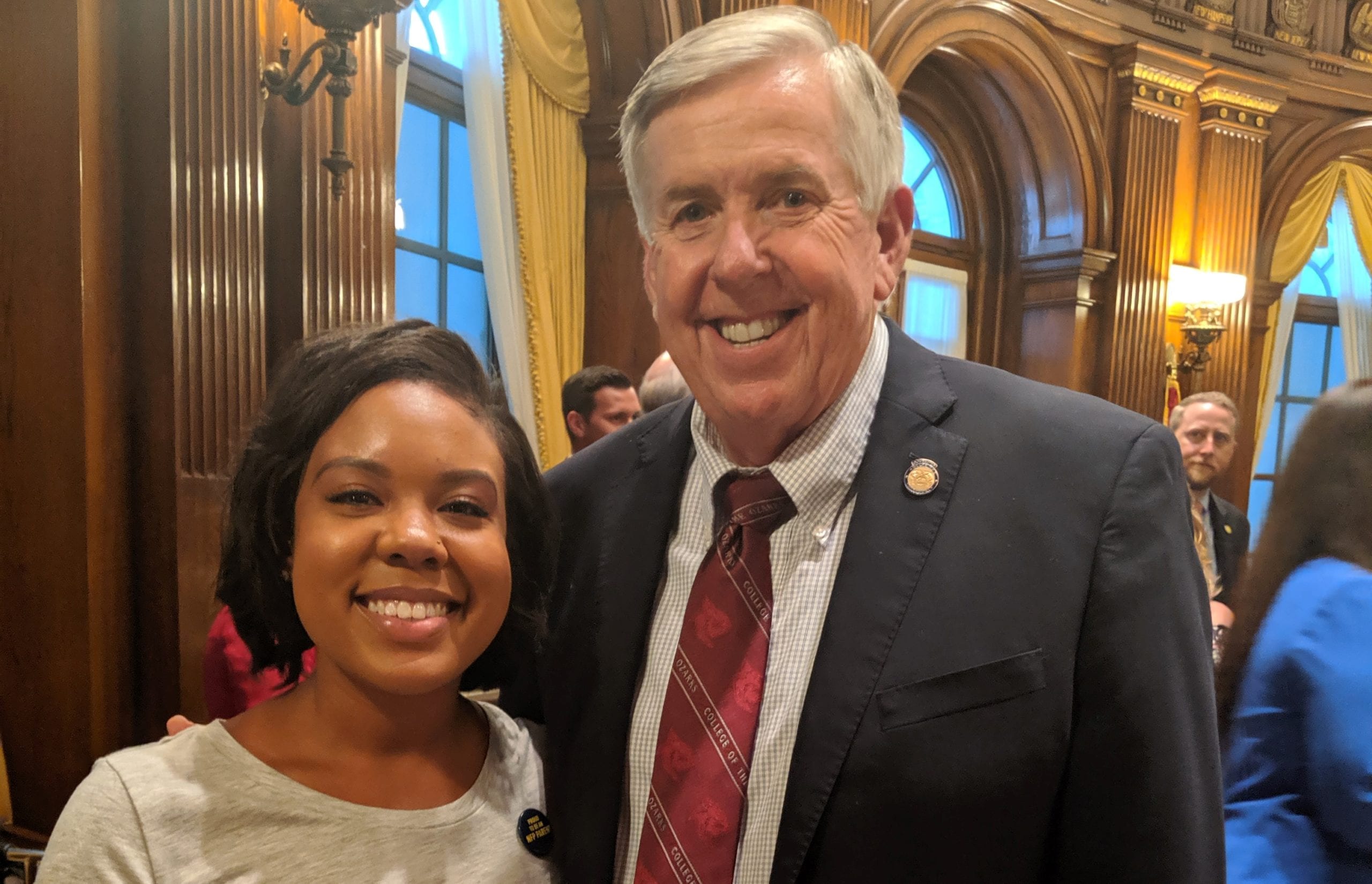 An adult with a light skin tone and an adult with a dark skin tone are standing side by side, smiling for a photo at an event.