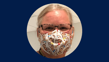 An adult with a light skin tone, wearing glasses and a face mask, is posing for a photo.