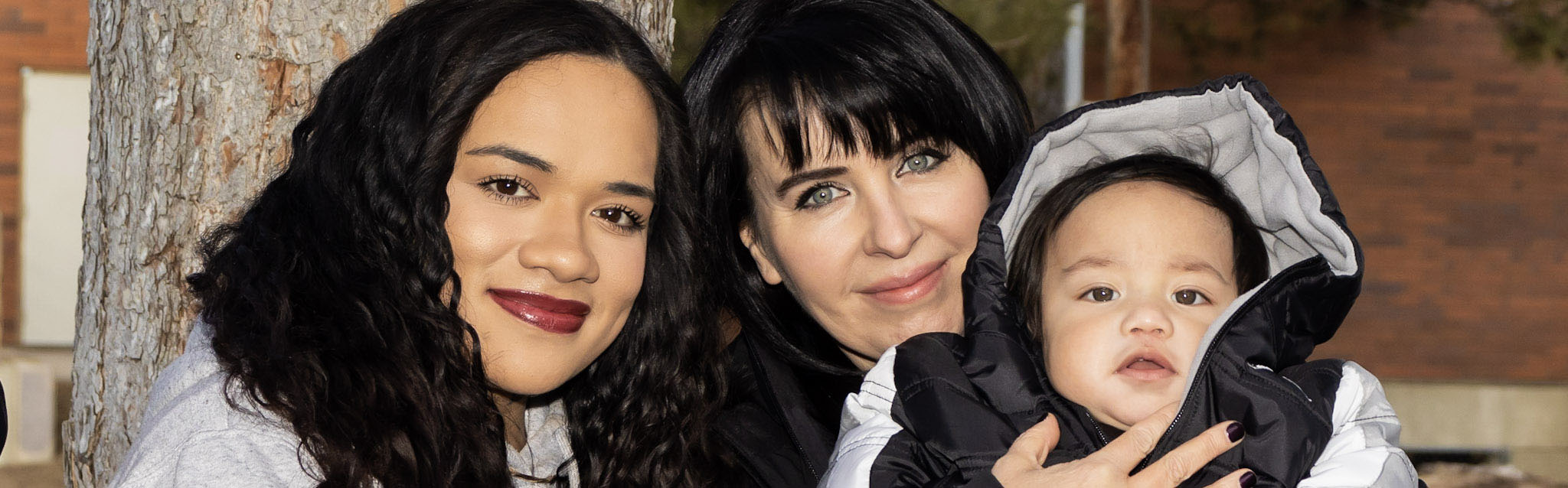 Two adults and a baby with a medium skin tone are smiling happily together.