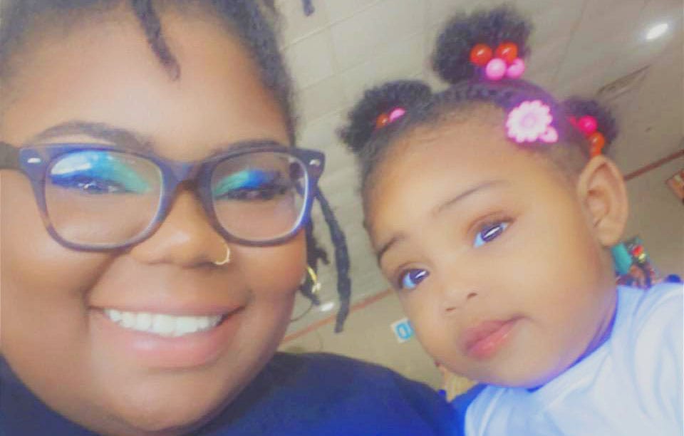 An adult and baby, both with a dark skin tone, are taking a selfie with a playful filter applied.