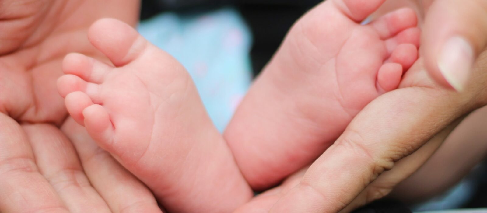 A baby with a light skin tones feet are held in an adults hands with a light skin tone