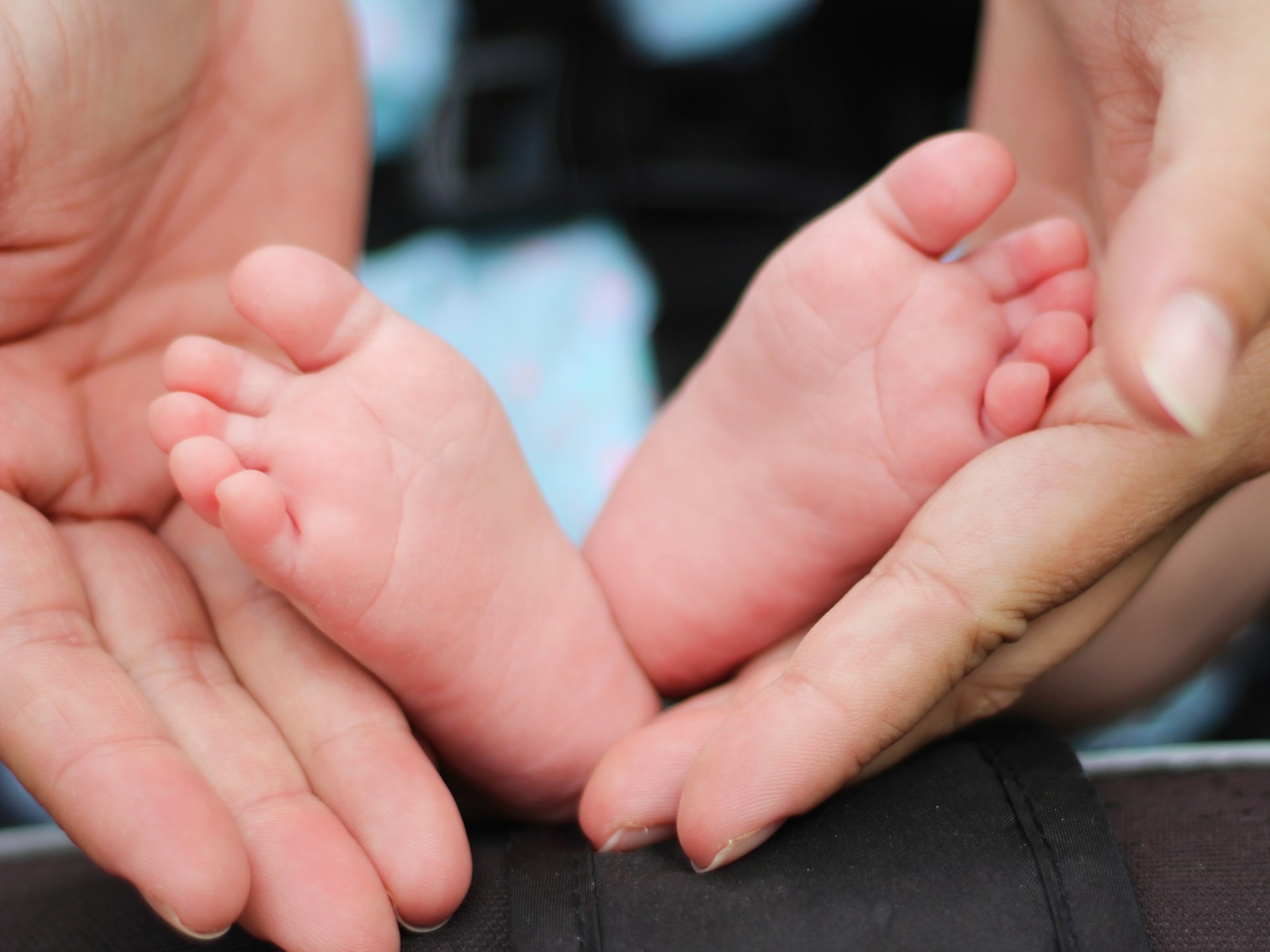 A baby with a light skin tones feet are held in an adults hands with a light skin tone