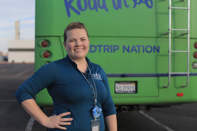 A Nurse-Family Partnership staff member with a light skin tone is smiling for a photo while standing in front of a bus.