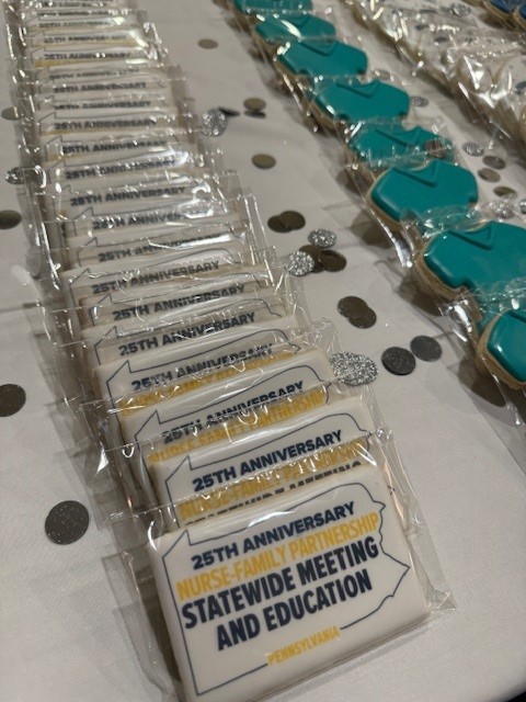 A line of cookies shaped like nurse scrub tops, with another cookie featuring the text "25th Anniversary Nurse-Family Partnership Statewide Meeting and Education."