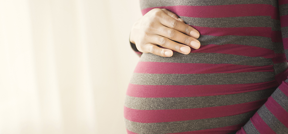 An adult with a dark skin tone places a hand on their baby bump