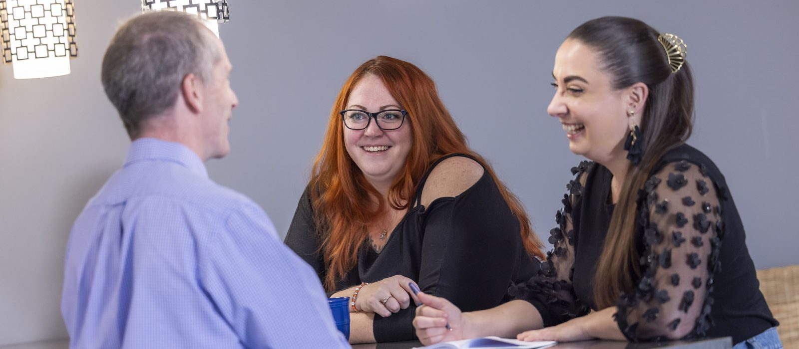 A group of three adults with light skin tones sit together in a room, sharing a laugh during a conversation.