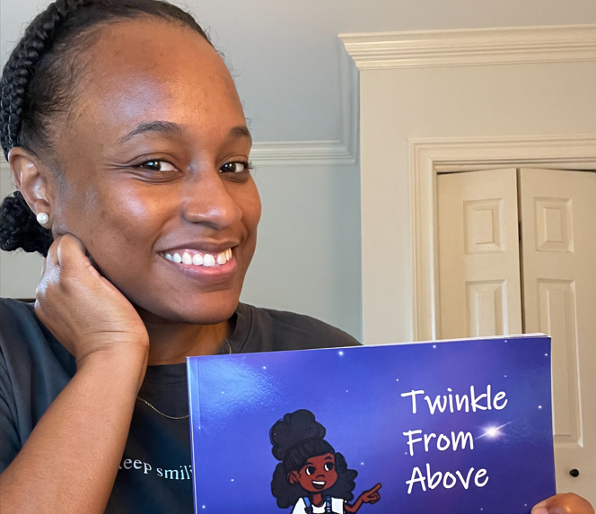 An adult with dark skin is holding the book Twinkle From Above, smiling for the camera.