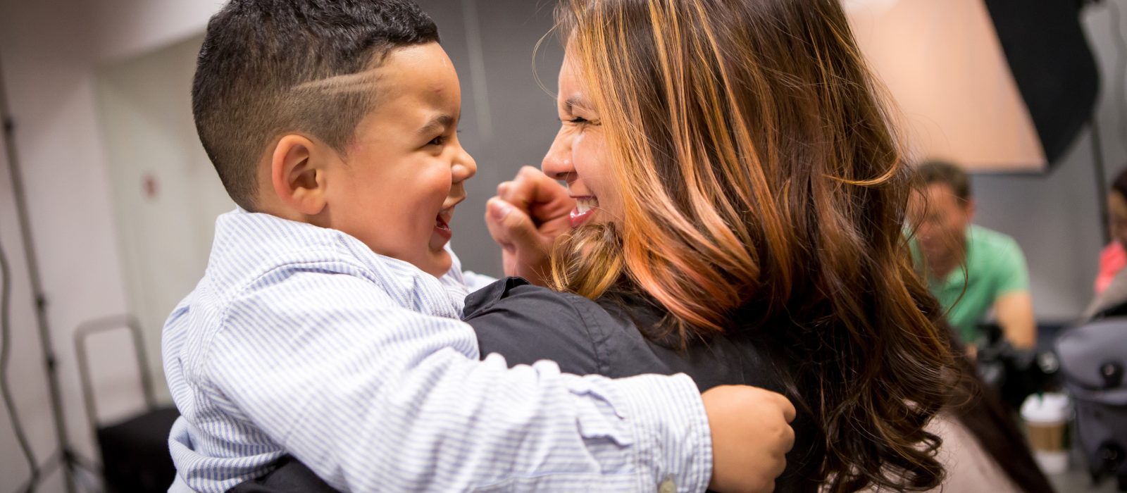 Adult holding a child smiling at each other, both have a medium skin tone